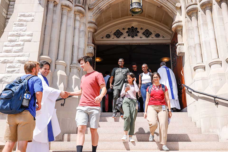 Students walking down the steps of College Church being greeted by a priest