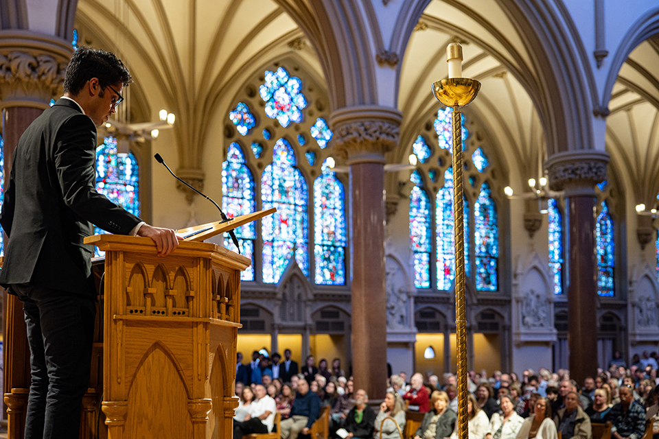 A male student addresses an audience from a podium inside a church. 